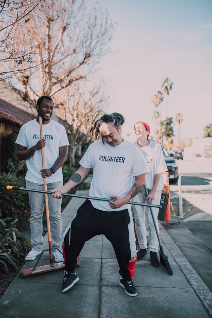 Three diverse volunteers laugh and clean a street, promoting community engagement.